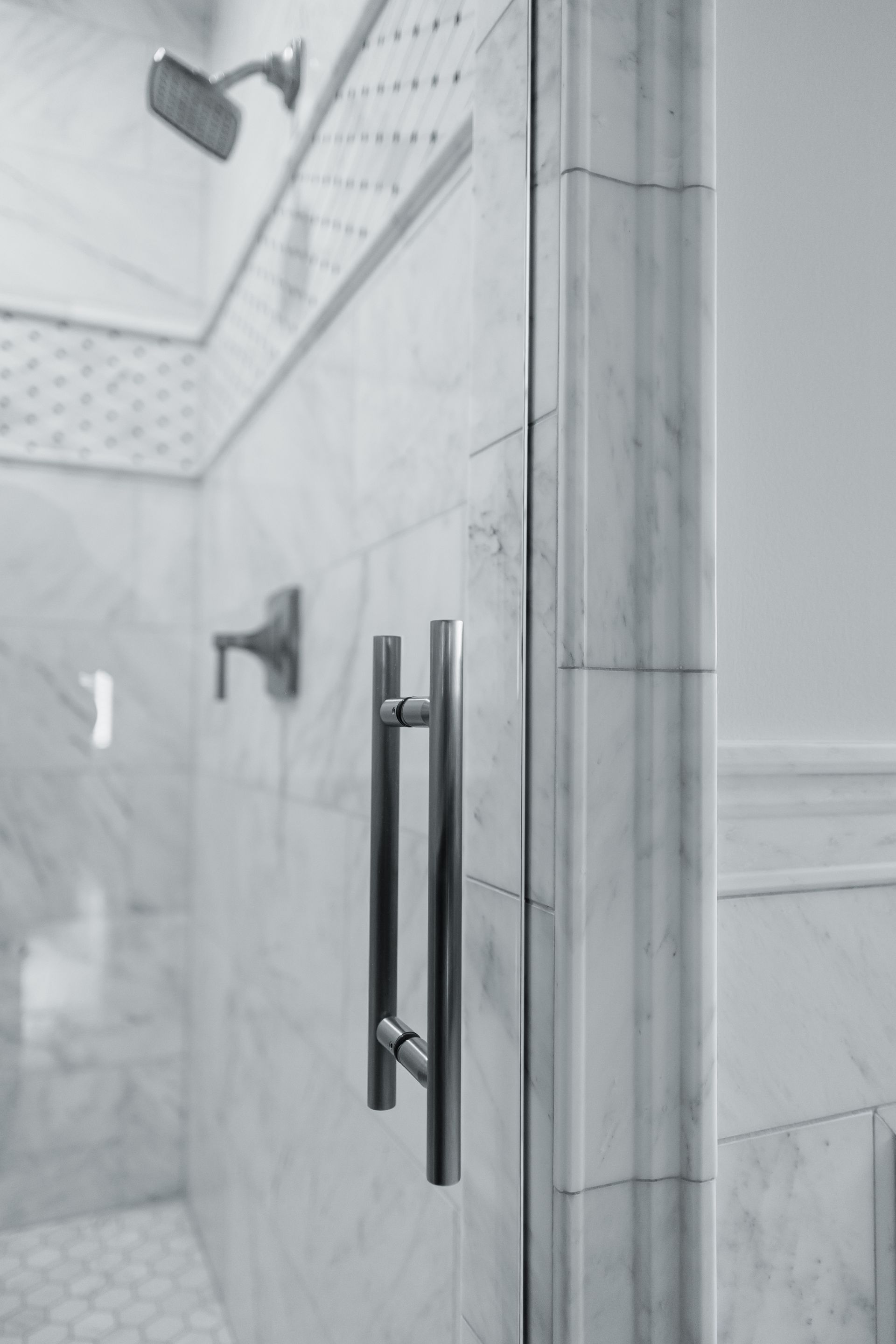 Newly tiled shower stall with marble-like white and gray tiles, built-in seat and niche, and a glass door frame.