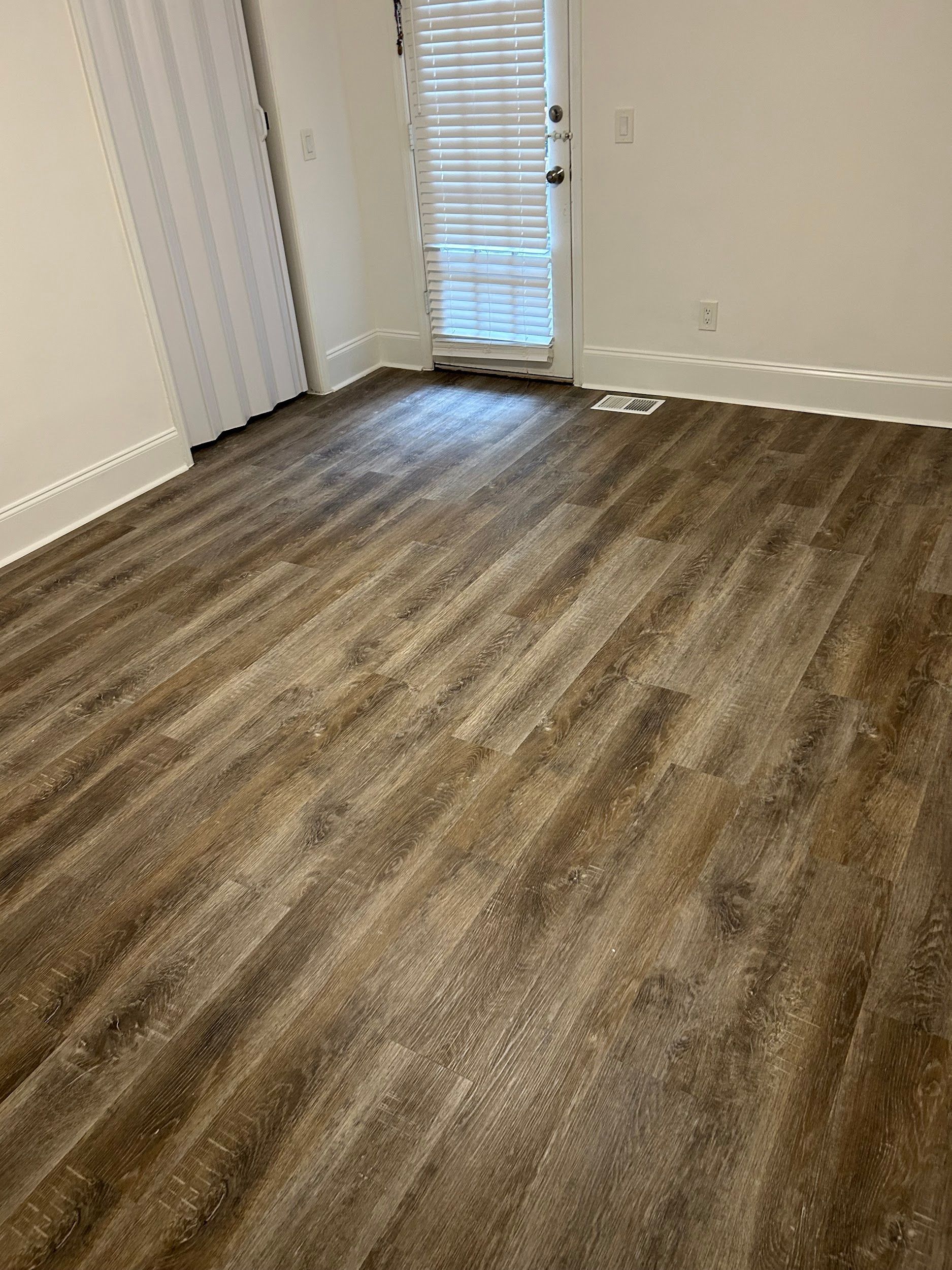 Brown wood-look flooring in a room with white walls, door to the outside, and a white curtain.