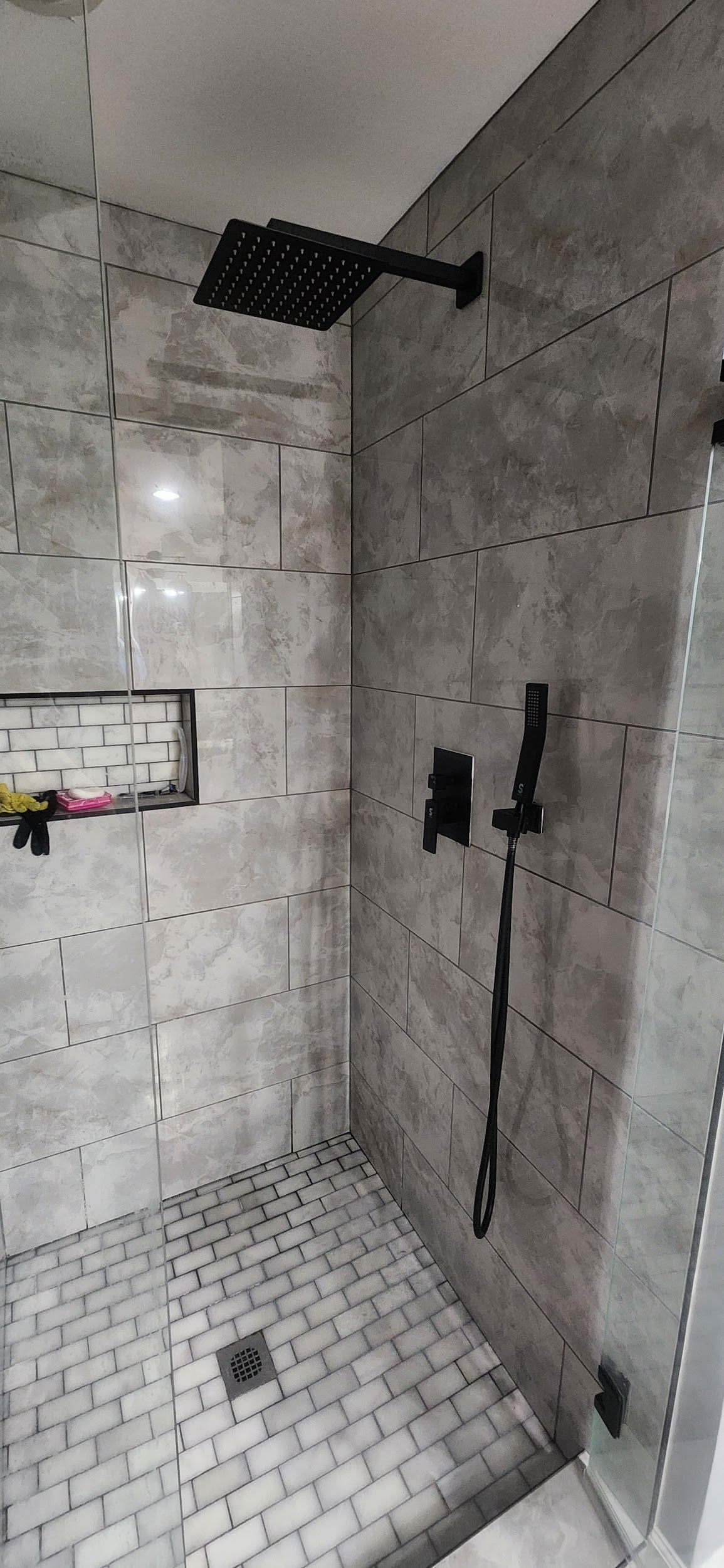 Black shower fixture in a tiled shower stall.