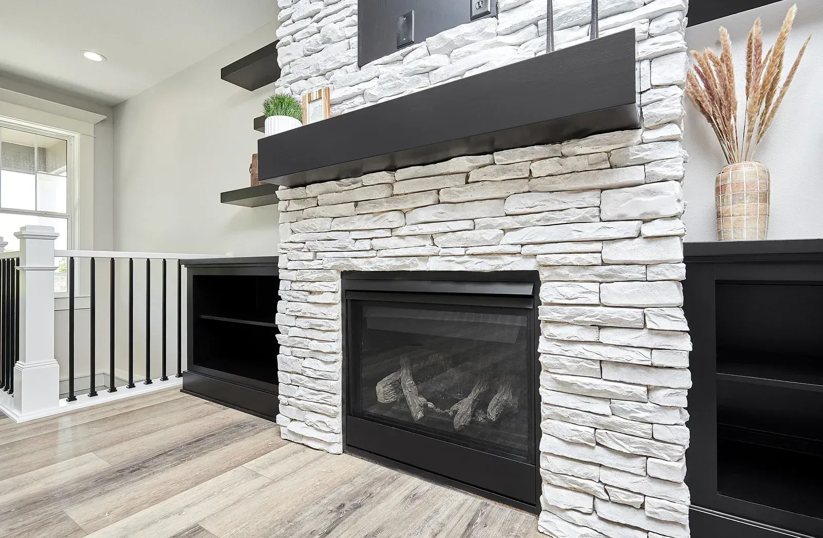 Fireplace with stacked stone surround, black mantel, and built-in shelving.