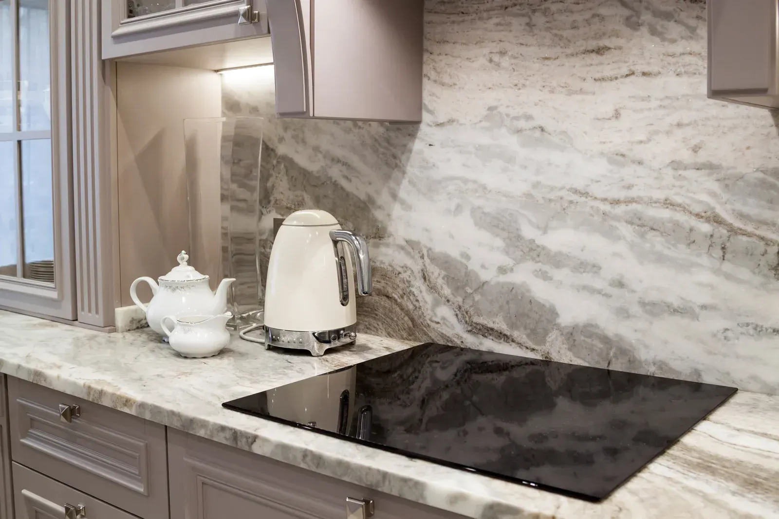 Kitchen counter with built-in stovetop, teapot, electric kettle, and gray marble backsplash.