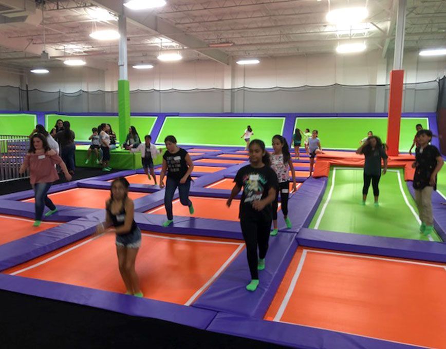 Children jumping and running on connected trampolines inside a brightly lit indoor trampoline park.