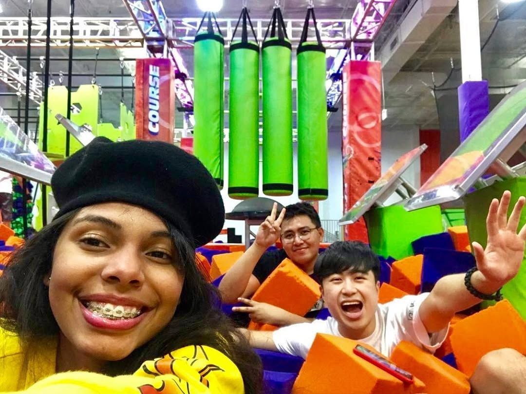 Three people smiling in an indoor adventure park. Woman in a beret takes a