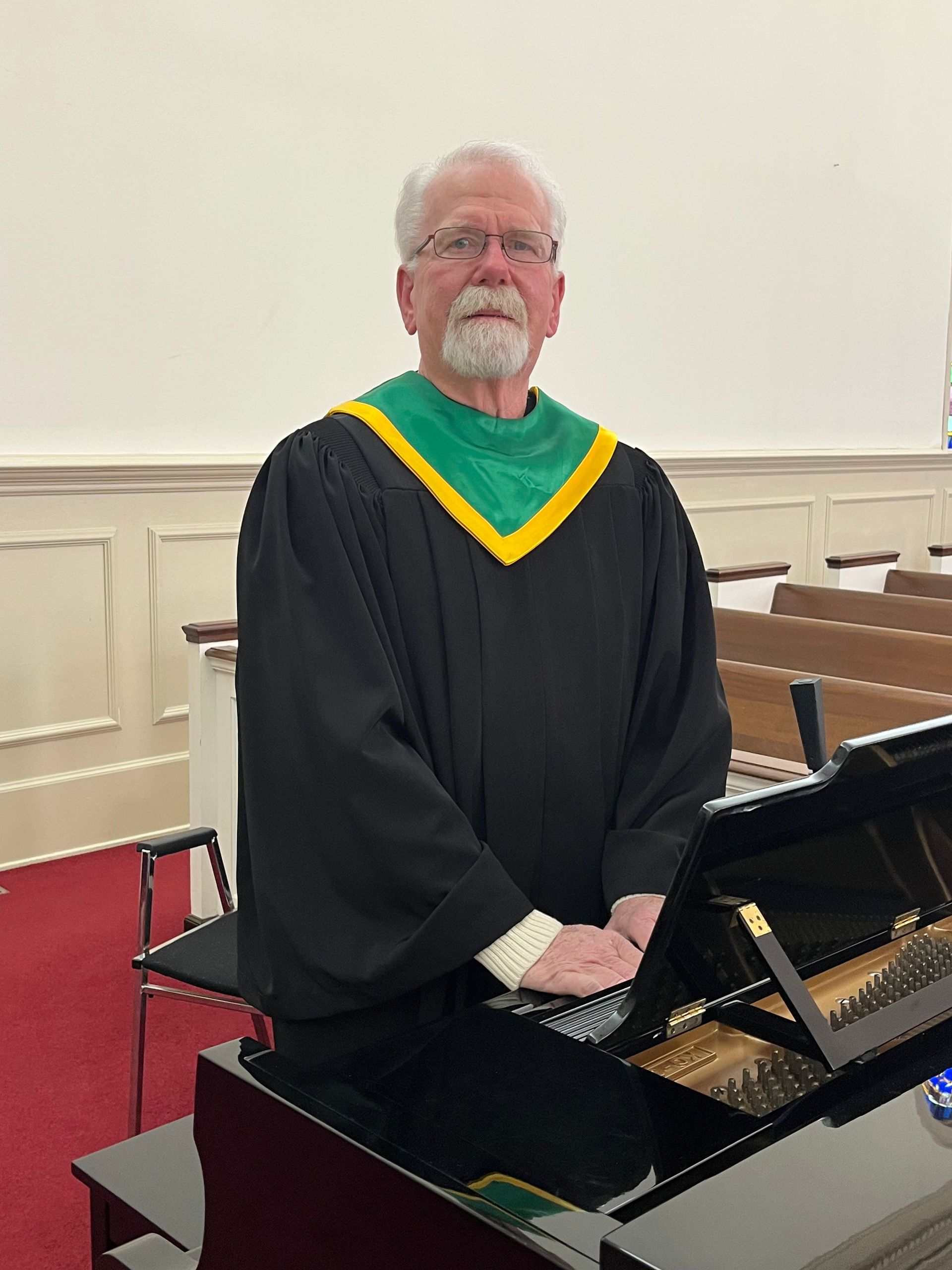 A man in a black robe is standing in front of a piano.