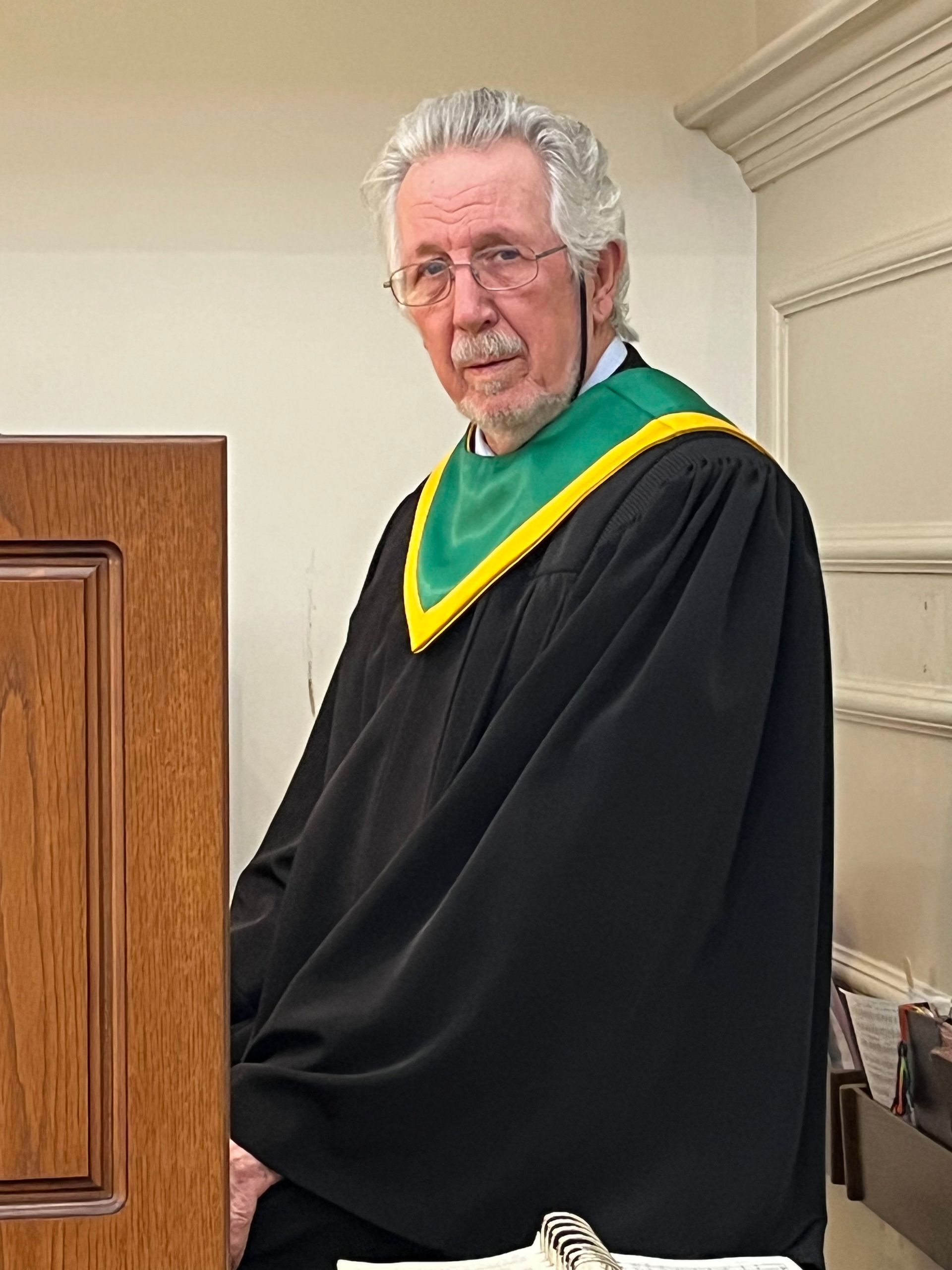 A man in a black robe with a green and yellow scarf around his neck
