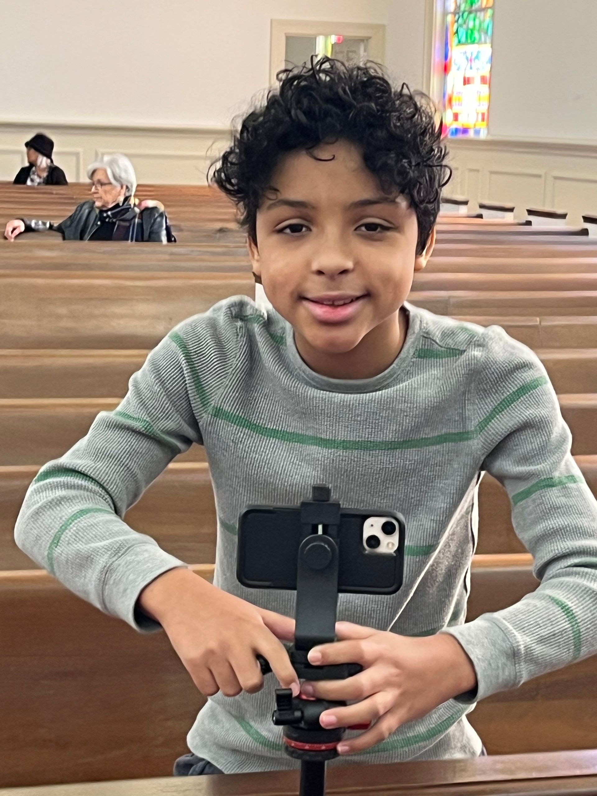 A young boy is holding a cell phone on a tripod in a church.