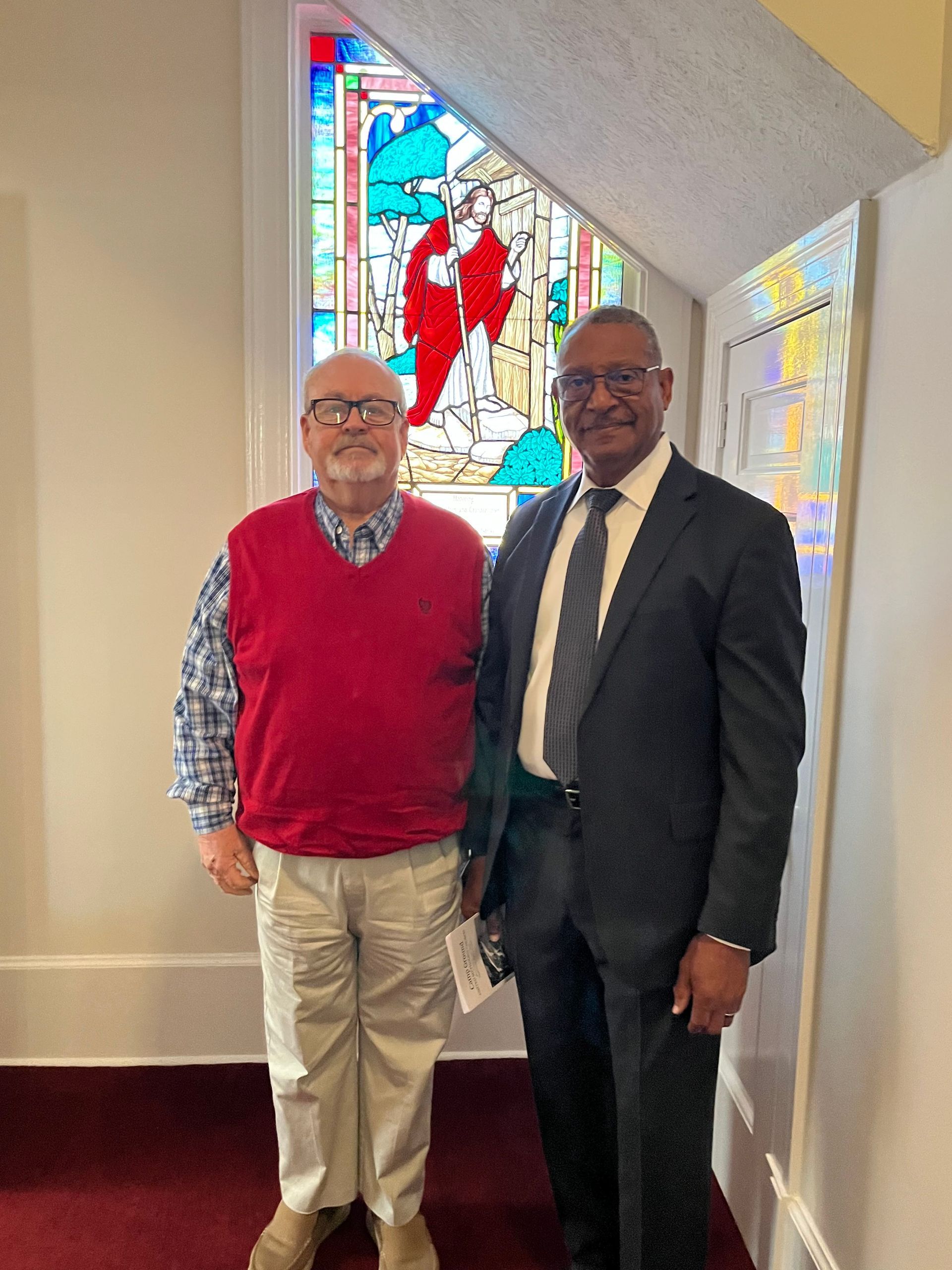 Two men are standing next to each other in front of a stained glass window.
