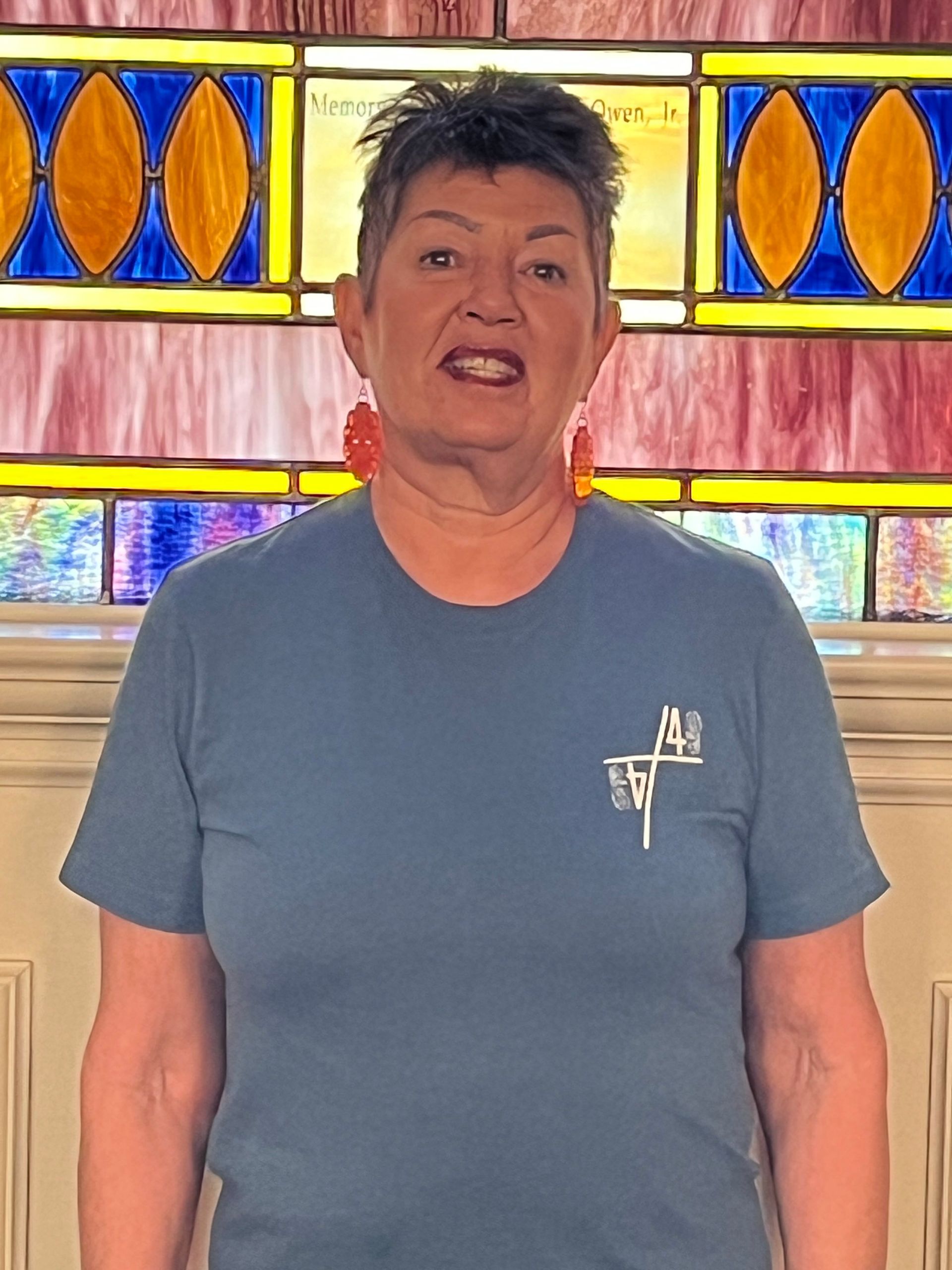 A woman in a blue shirt is standing in front of a stained glass window.