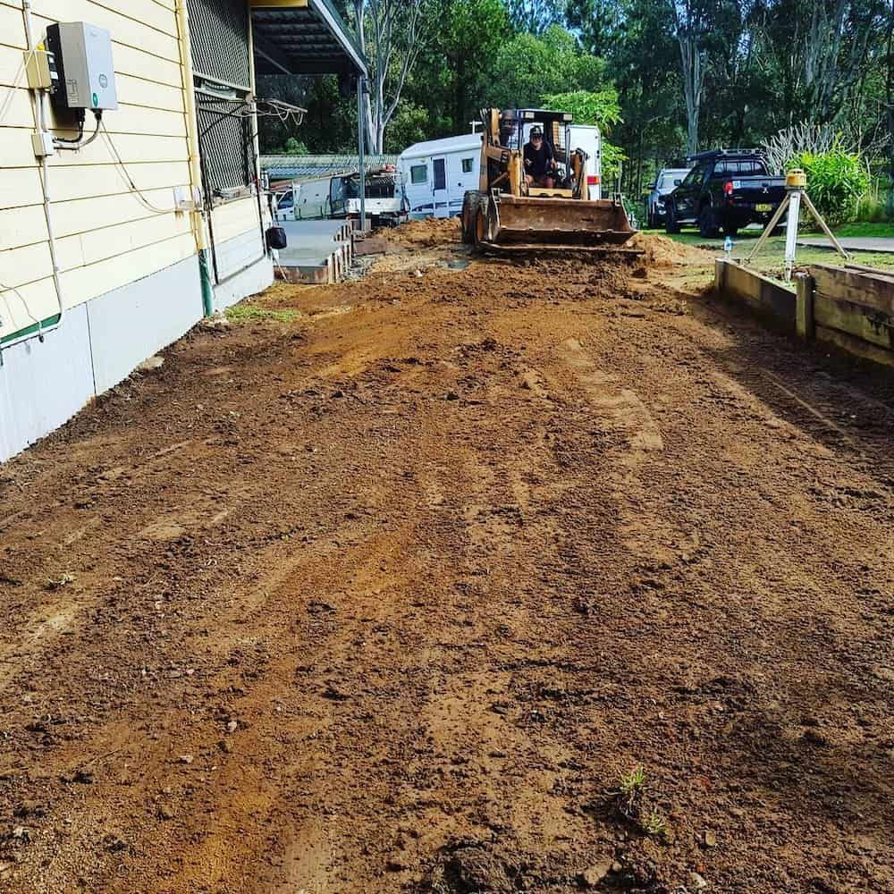 A Bulldozer is Moving Dirt in Front of a House — TJ Concreting in Ballina, NSW