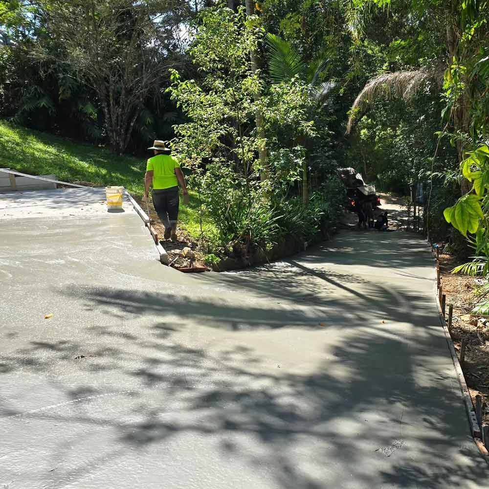 A Man in a Green Shirt is Walking Down a Concrete Driveway — TJ Concreting in Lismore, NSW