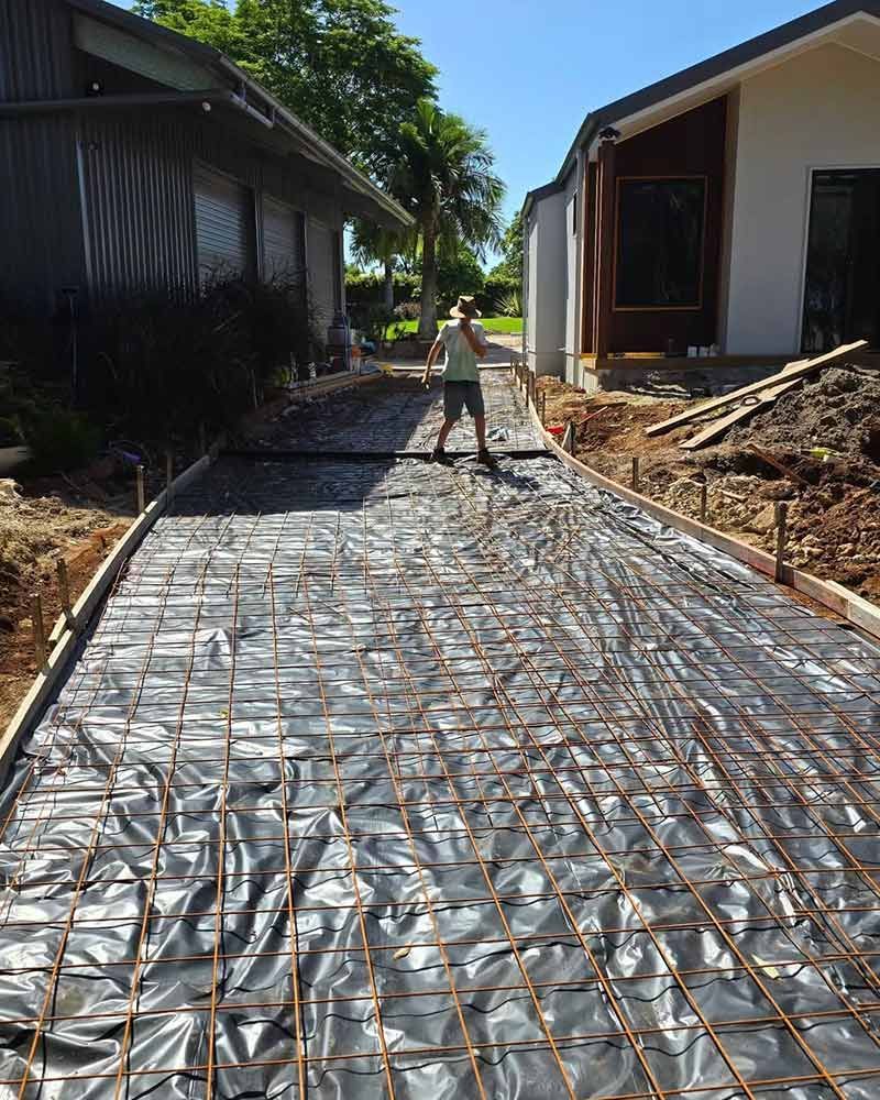 A Man is Standing on a Concrete Driveway in Front of a House — TJ Concreting in Lismore, NSW