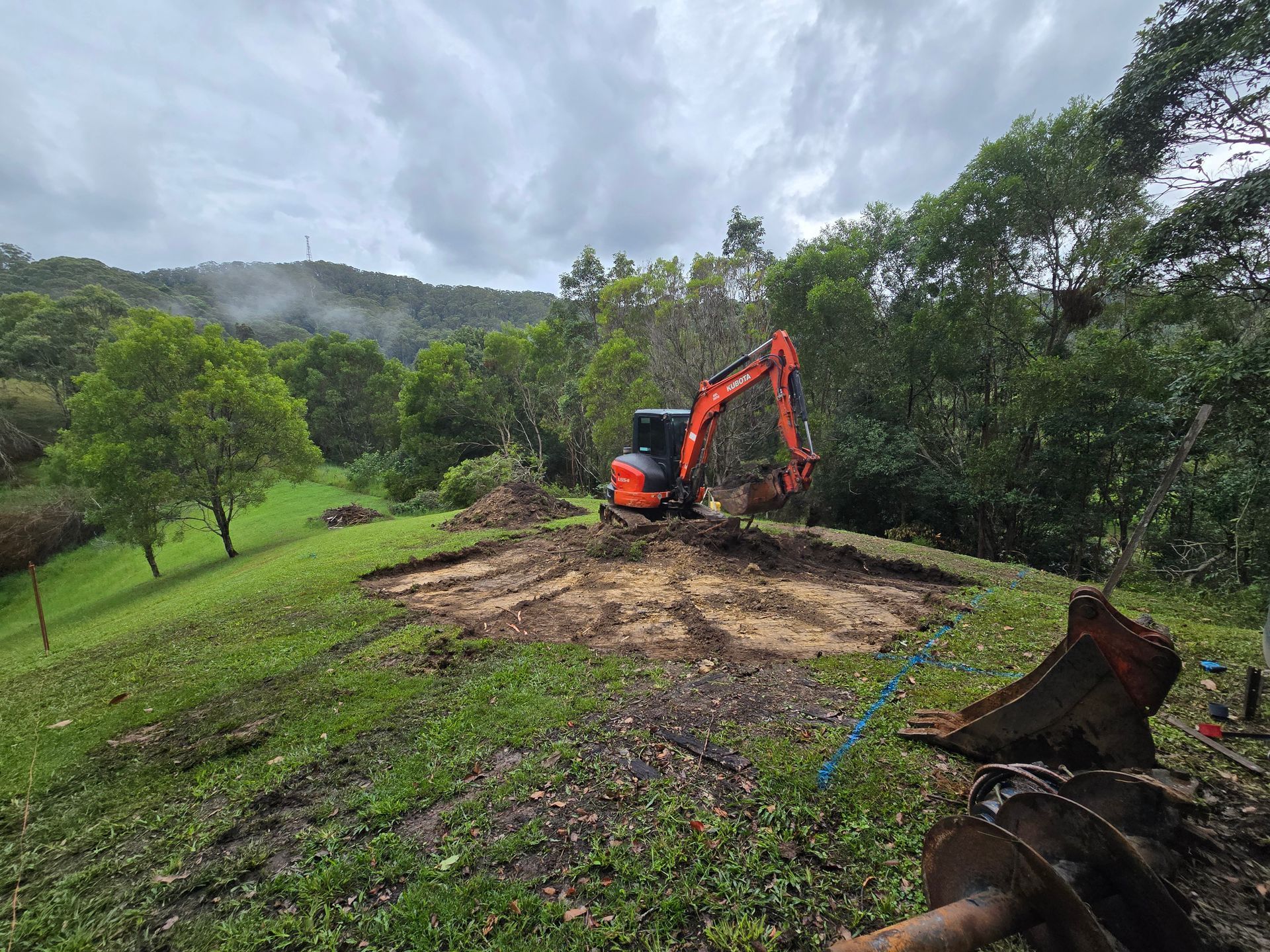 A Blue Excavator is Parked on the Side of a Road — TJ Concreting in Myocum, NSW
