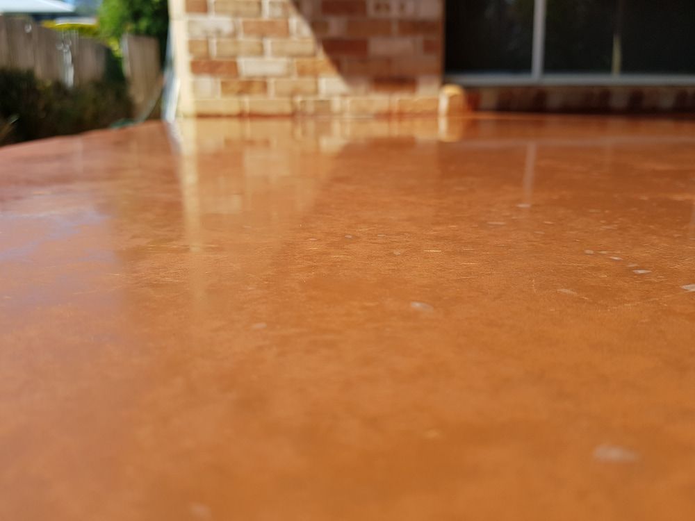 A Close Up of a Concrete Floor With a Brick Building in the Background — TJ Concreting in Myocum, NSW