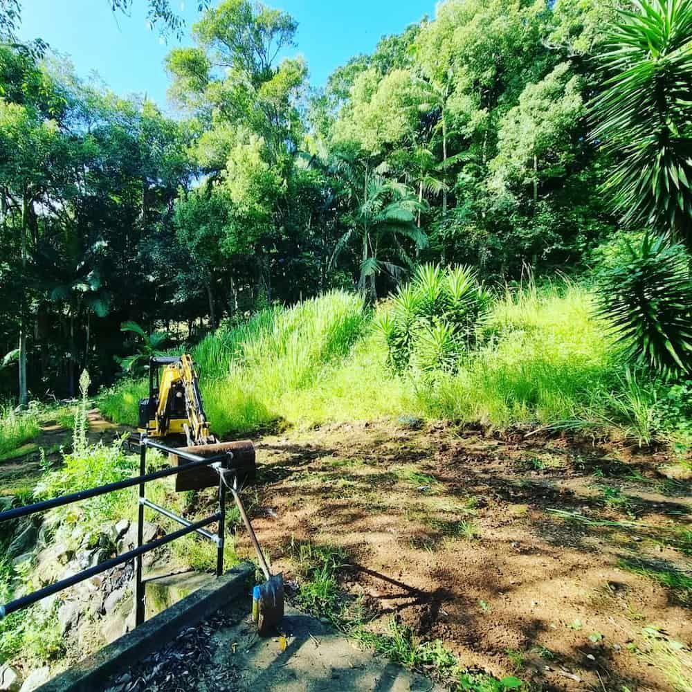 A Bulldozer is Sitting on Top of a Dirt Hill in the Middle of a Forest — TJ Concreting in Lismore, NSW