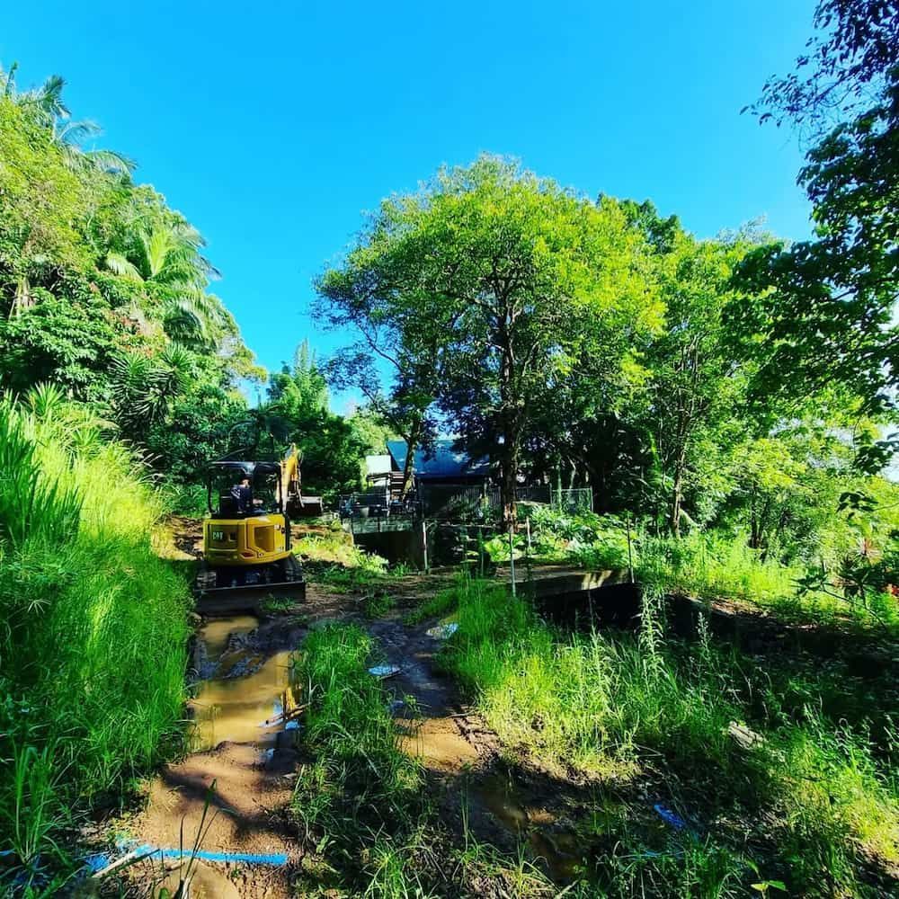 A Bulldozer is Driving Down a Dirt Road Surrounded by Trees — TJ Concreting in Federal, NSW