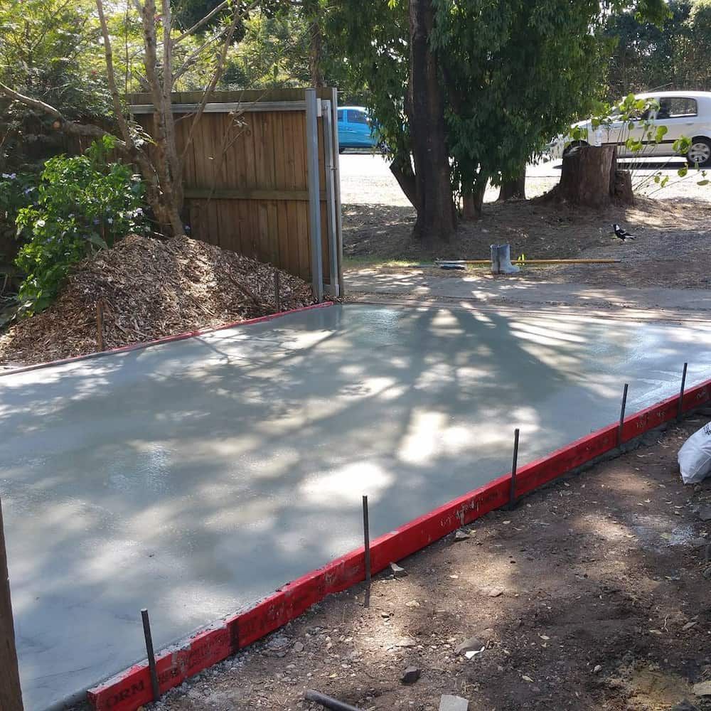 A Concrete Driveway With a Red Curb and a Wooden Fence in the Background — TJ Concreting in Ballina, NSW