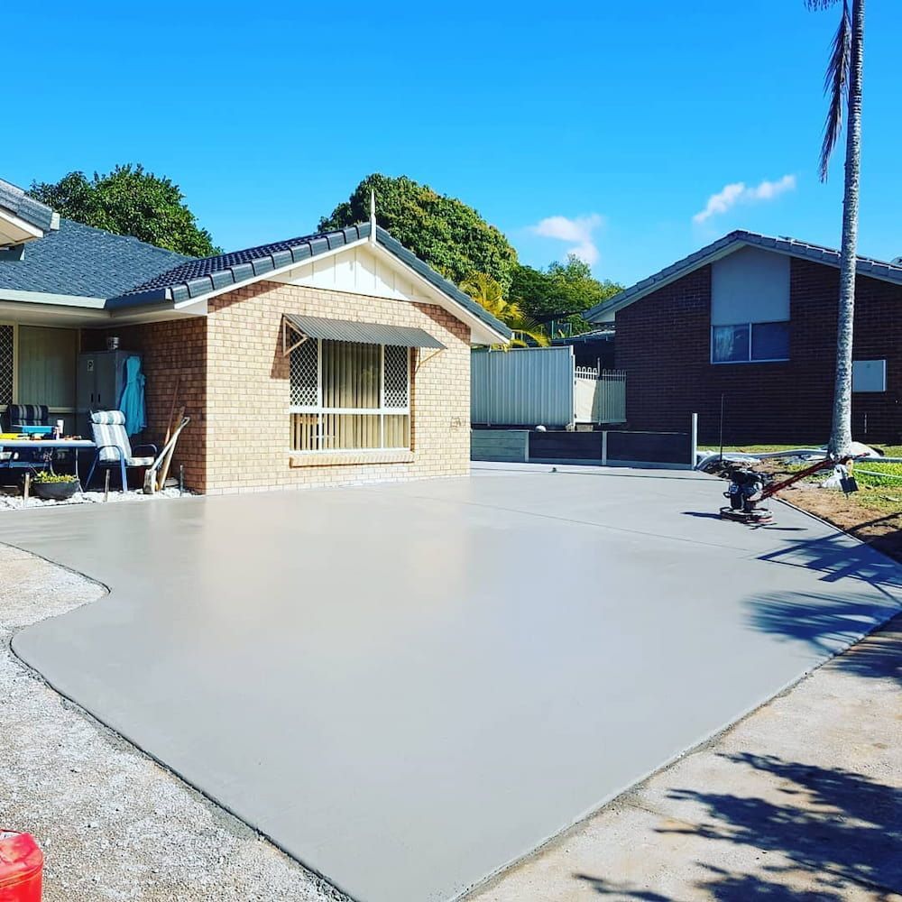 A Brick House With a Concrete Driveway in Front of It — TJ Concreting in Bangalow, NSW