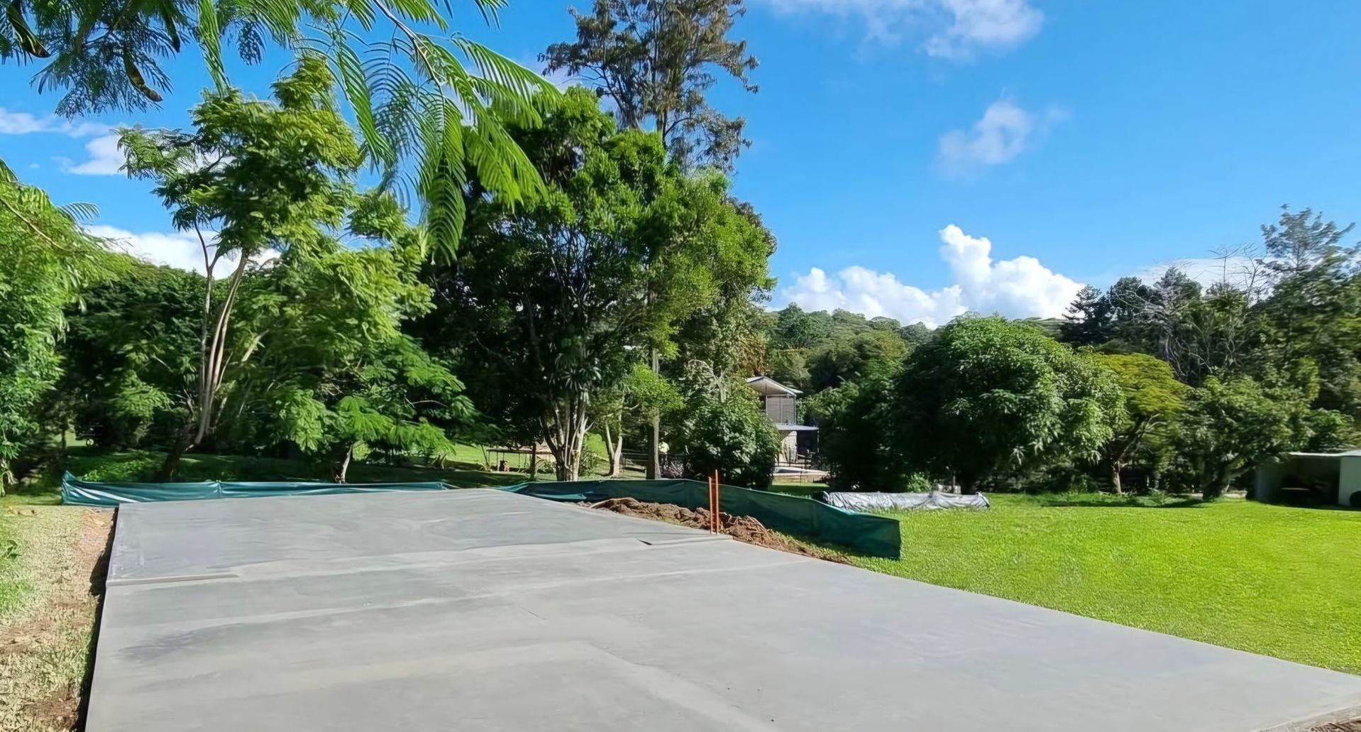 A Concrete Driveway is Surrounded by Trees and Grass on a Sunny Day— TJ Concreting in Myocum, NSW