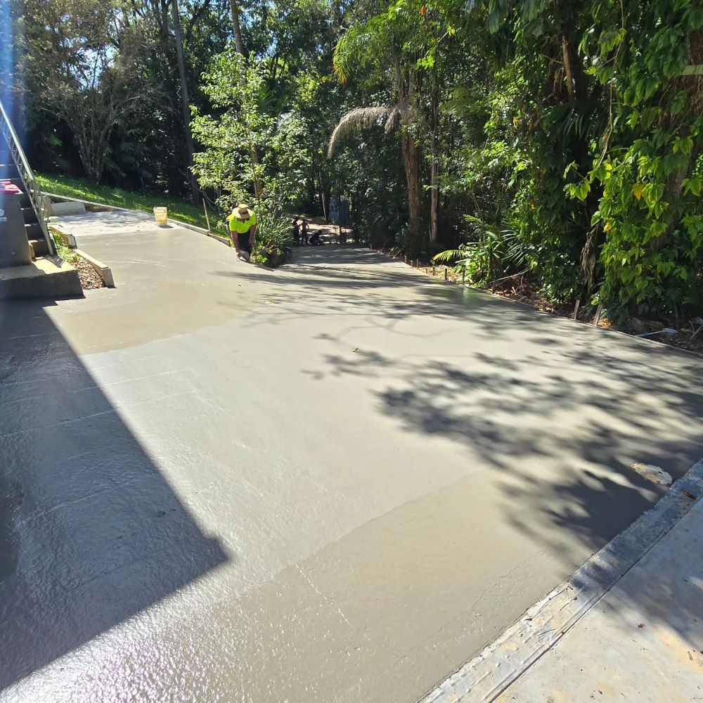 A Man is Fixing a Concrete Driveway Surrounded by Trees — TJ Concreting in Myocum, NSW