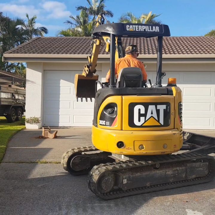 A Yellow Caterpillar Excavator is Parked in Front of a House — TJ Concreting in Myocum, NSW