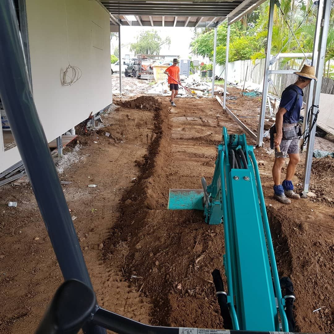 A Man is Standing Next to a Green Excavator in a Dirt Field — TJ Concreting in Myocum, NSW