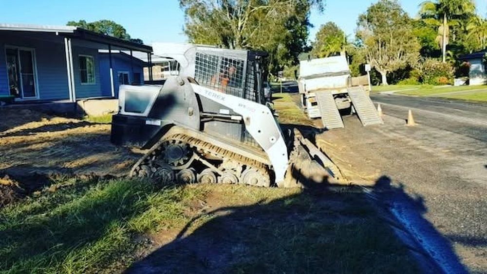 A Bulldozer is Parked on the Side of the Road in Front of a House — TJ Concreting in Murwillumbah, NSW