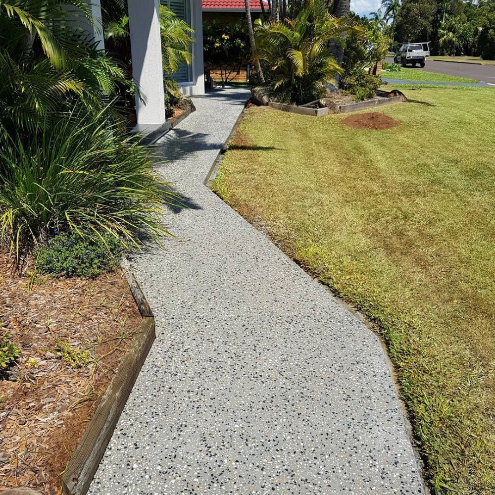 A Concrete Walkway Leading to a House Next to a Lush Green Lawn — TJ Concreting in Myocum, NSW