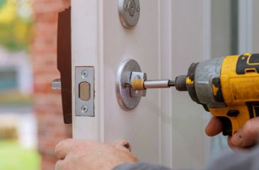 A person is installing a door lock with a drill.