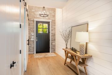 A hallway with a black door , a wooden table , a lamp and a mirror.