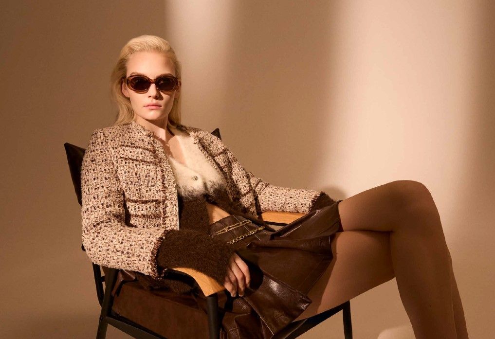 Una donna che indossa occhiali da sole è seduta su una sedia con le gambe incrociate.