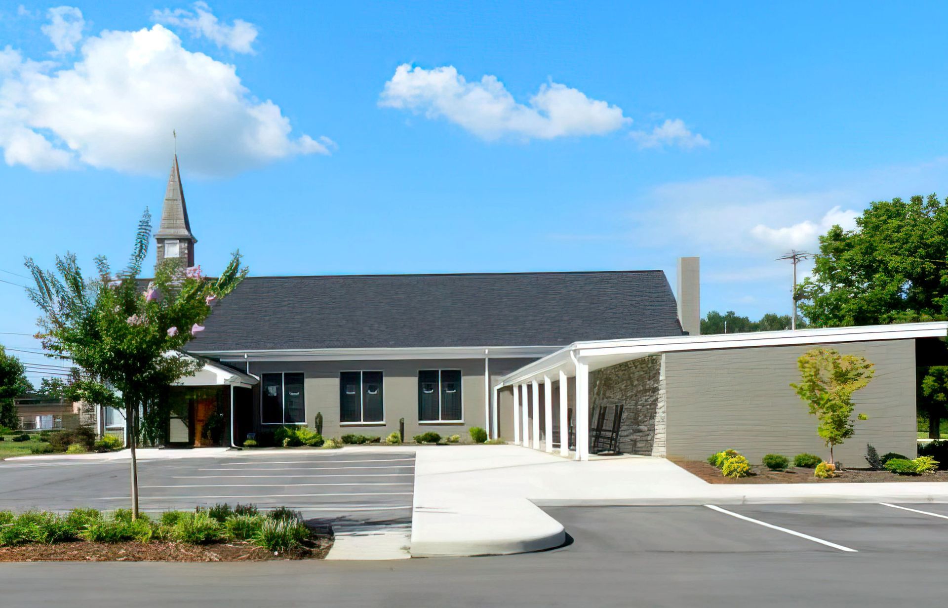 A church with a steeple and a parking lot in front of it