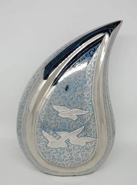 A silver vase with birds on it is sitting on a white surface.