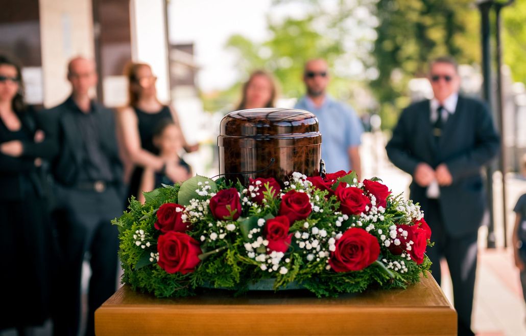 A urn surrounded by yellow roses and leaves on a table.