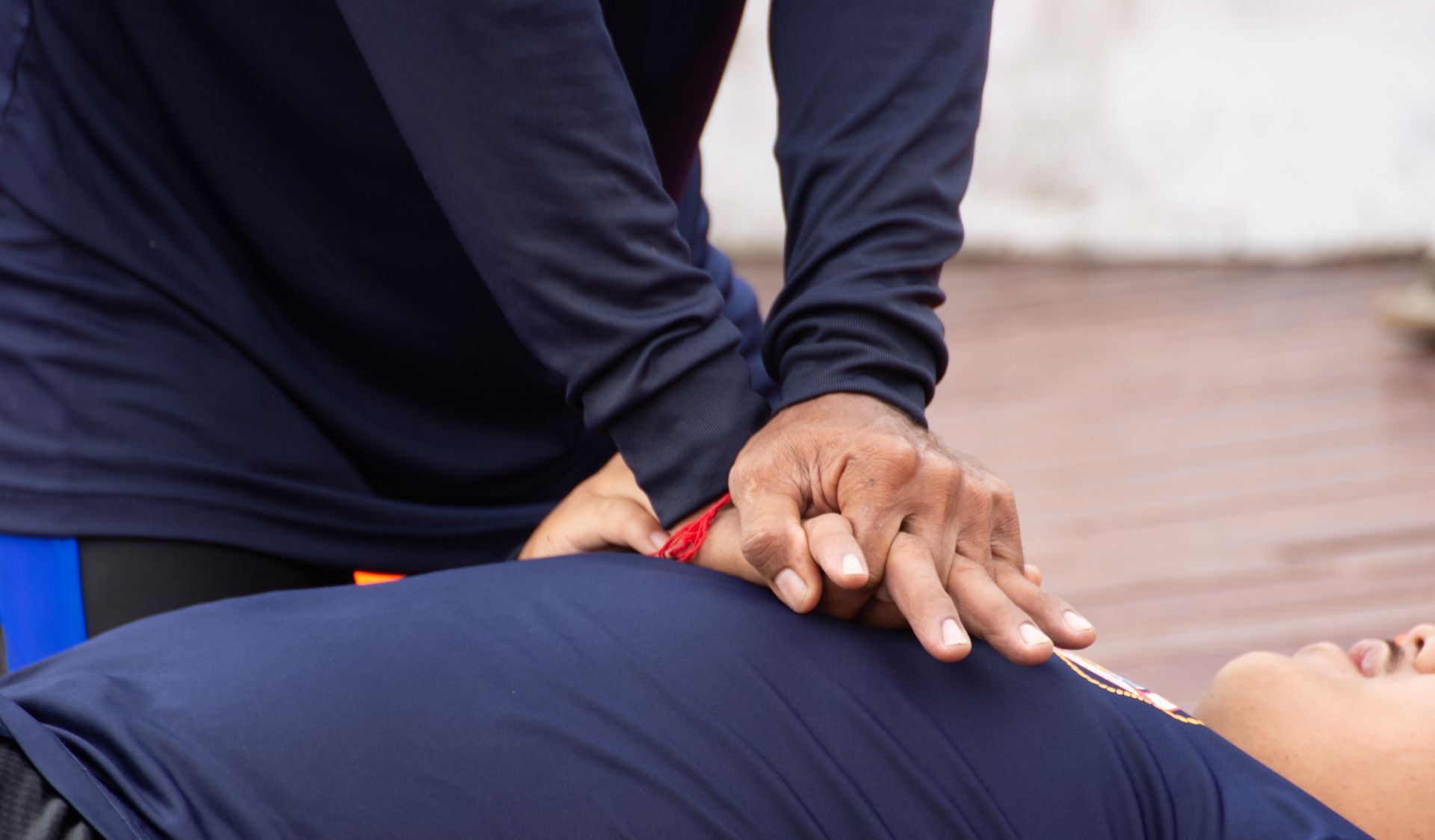 Person giving CPR to someone on the ground; hands on chest, navy blue clothing.