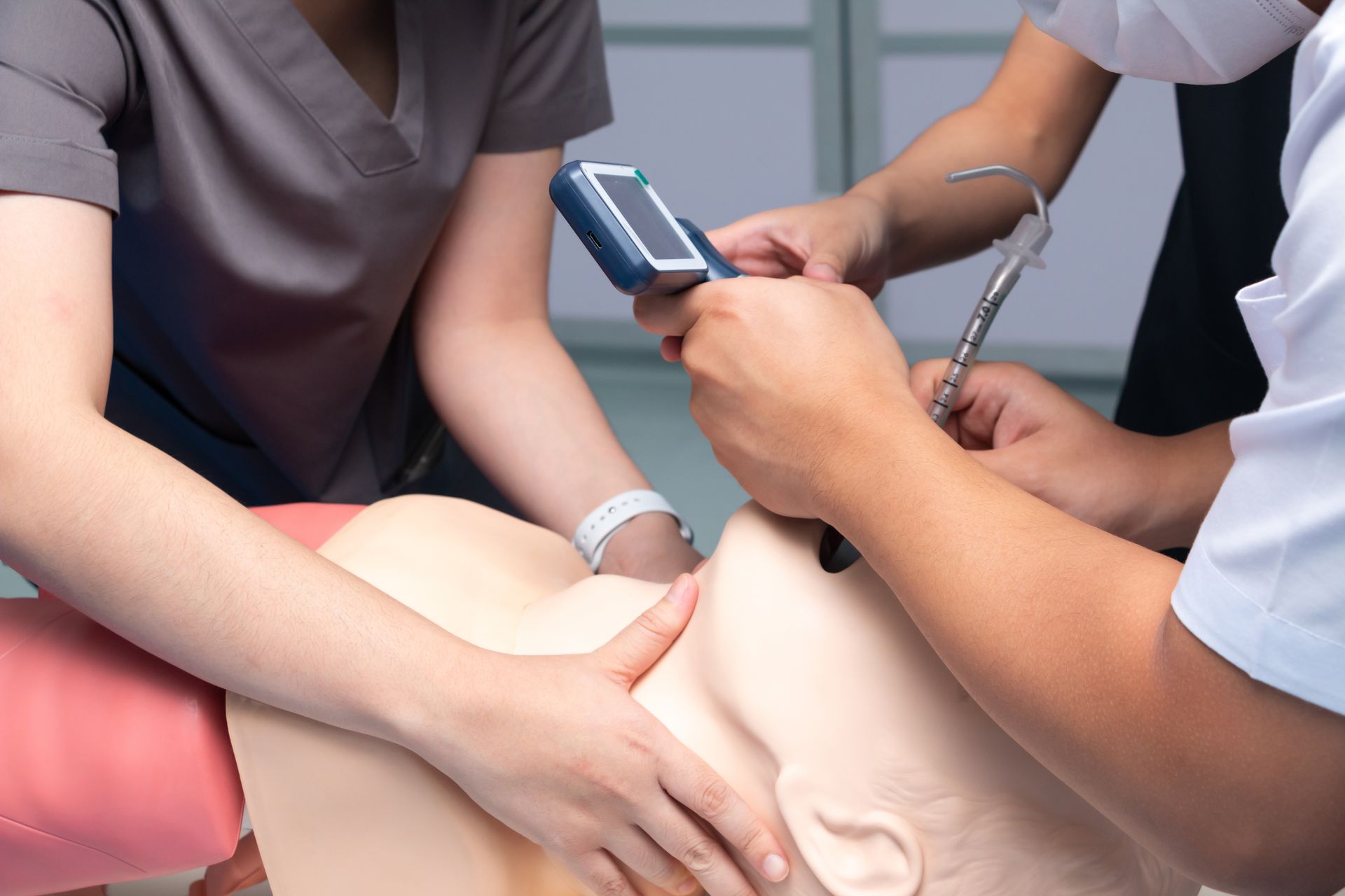 Medical professionals practice intubation on a training dummy, using a laryngoscope and monitor.