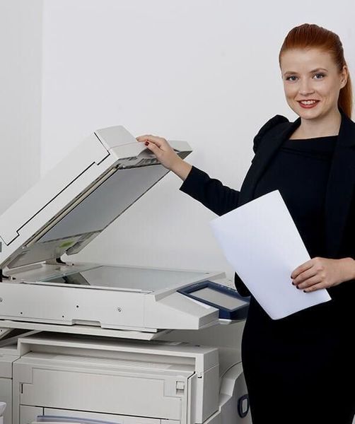 Una mujer está parada frente a una impresora sosteniendo un trozo de papel