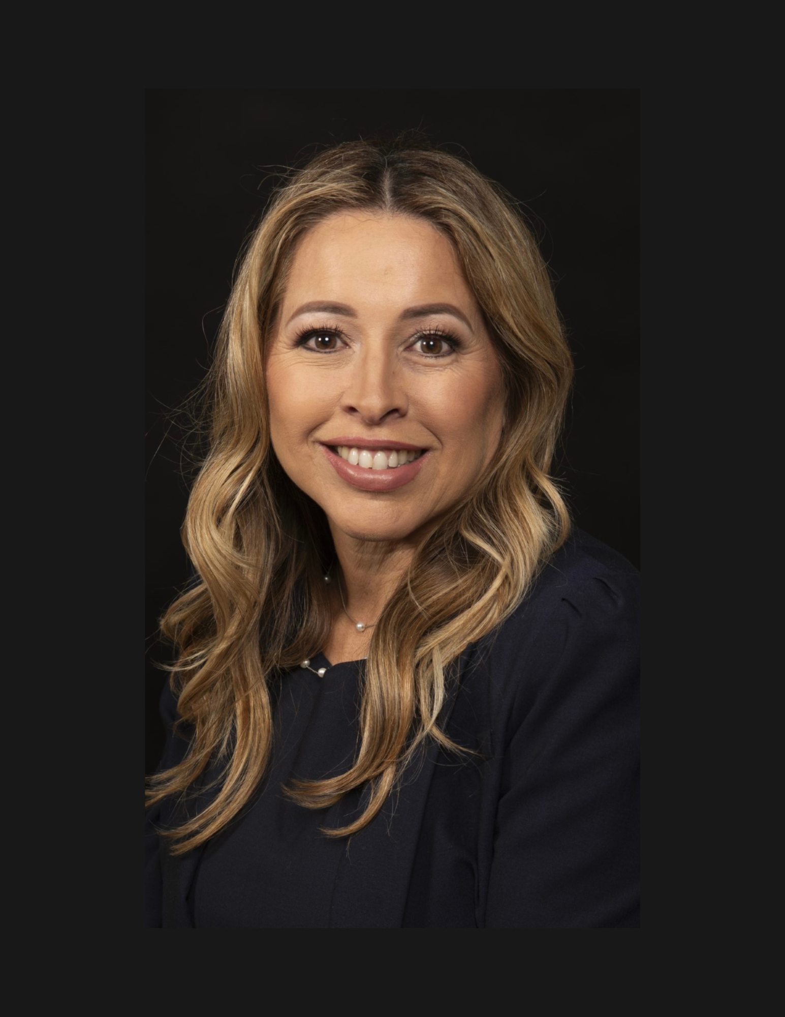 A woman with long blonde hair is smiling in front of a black background.