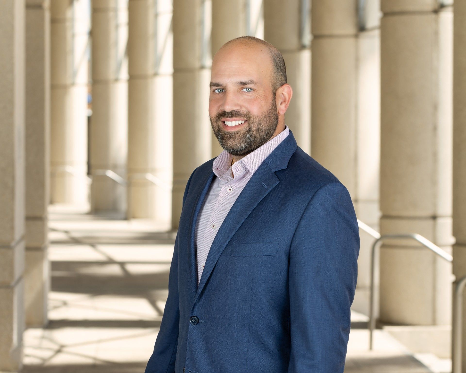 A man in a blue suit and pink shirt is standing in front of columns.
