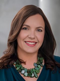 A woman wearing a green necklace and a blue shirt is smiling.