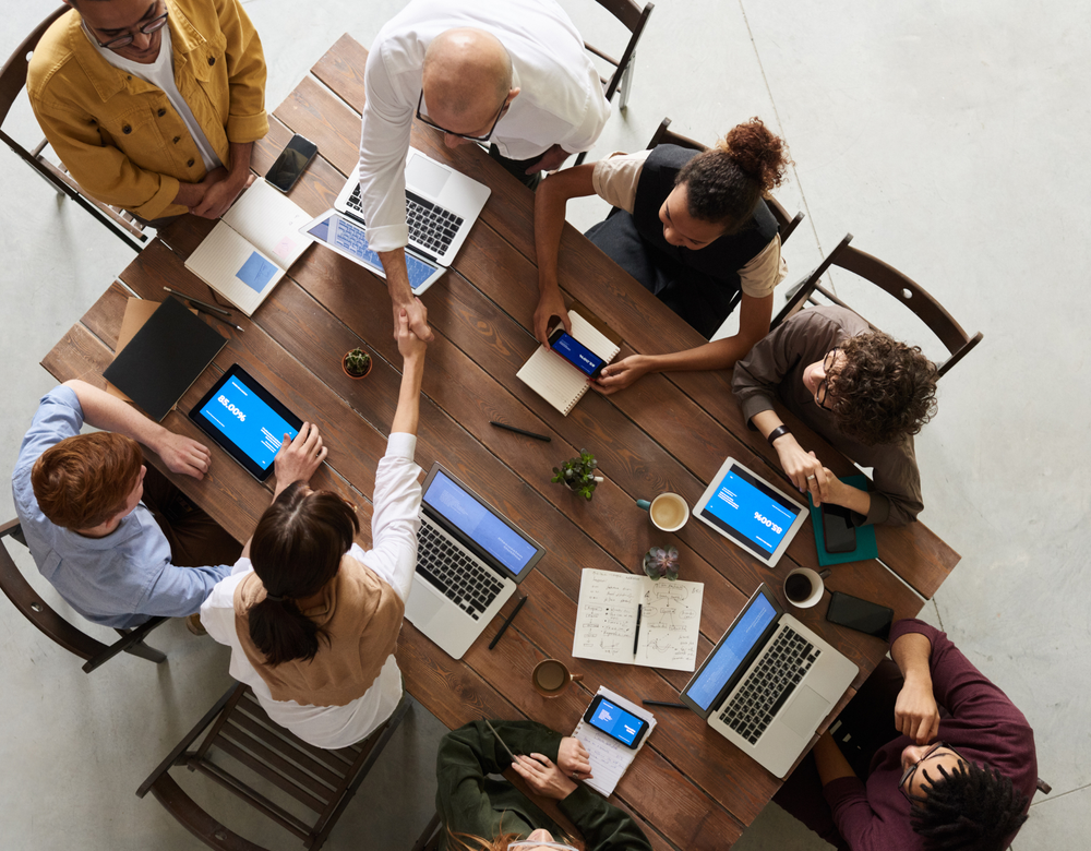 A group of people are sitting around a table shaking hands.