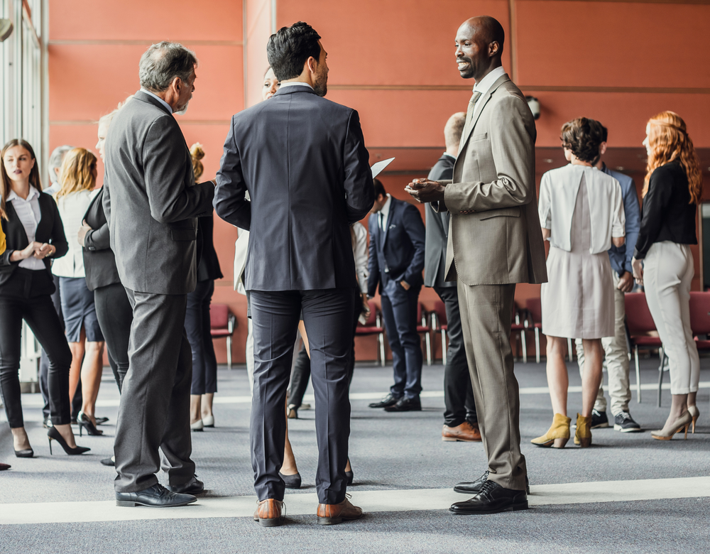 A group of business people are standing in a room talking to each other.