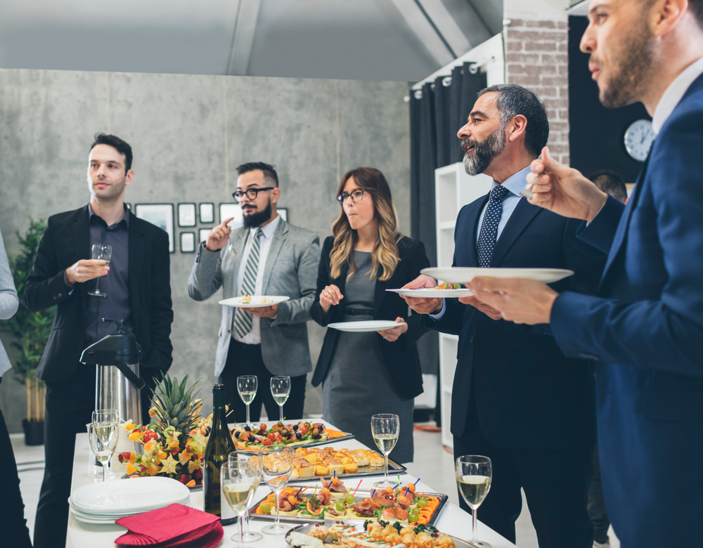 A group of people are standing around a table eating food.