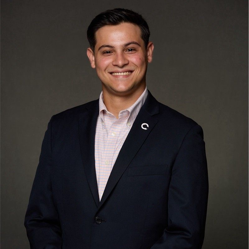 A man wearing a suit and a pink shirt with a c on his jacket