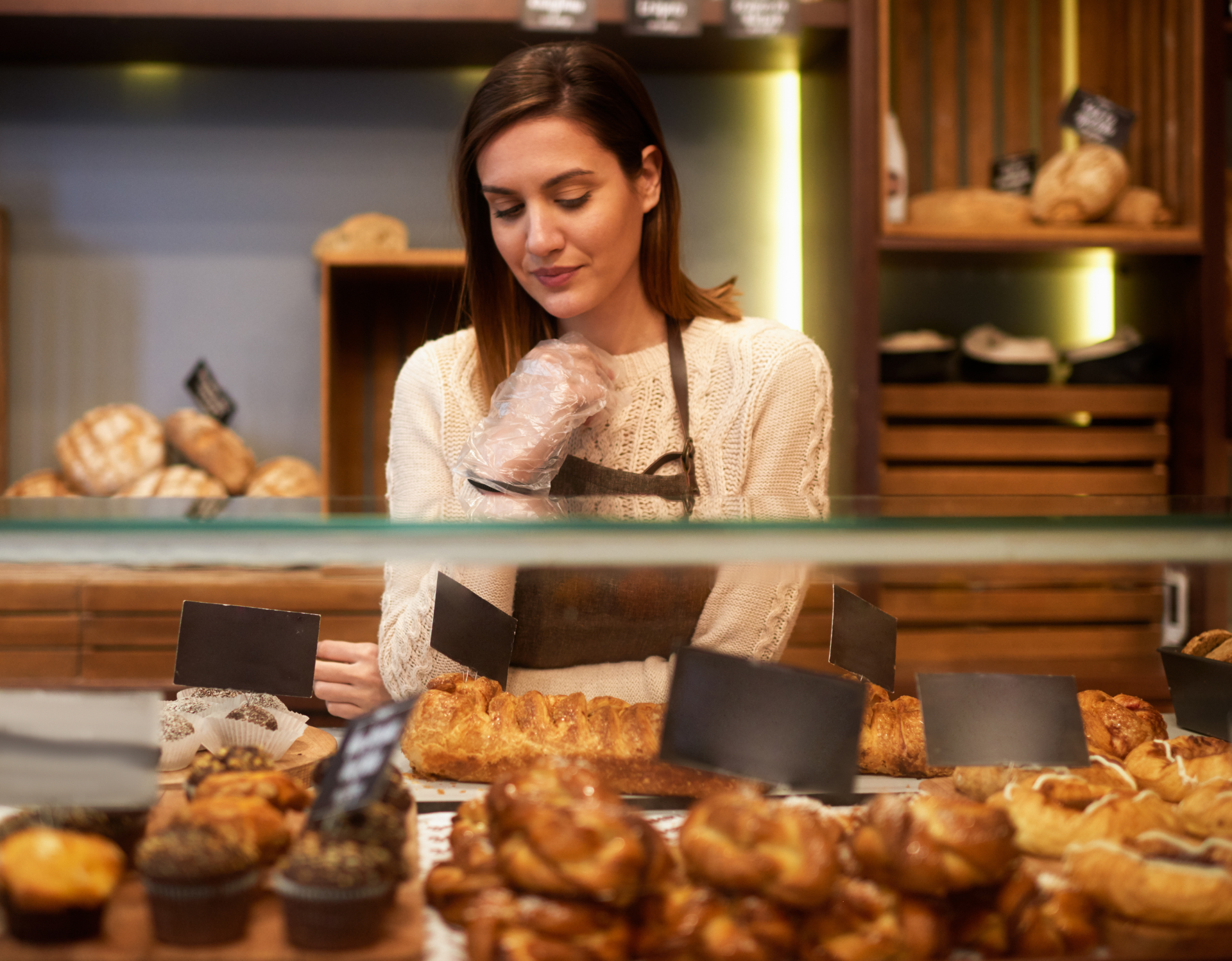 A woman is standing behind a glass display case in a bakery.