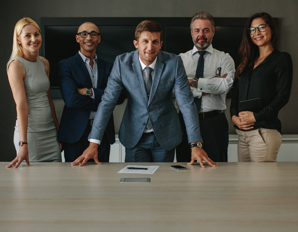 A group of business people are standing around a conference table.