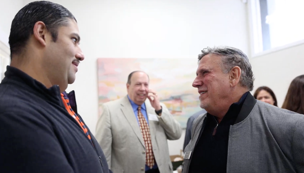 A group of men are standing in a room talking to each other.