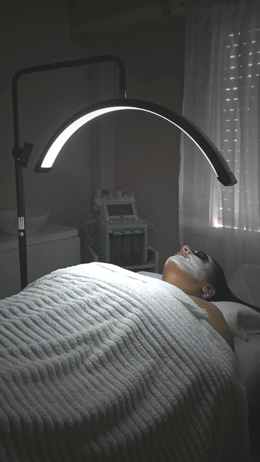 Una persona recibe un tratamiento facial profesional en un spa, bajo una luz LED 