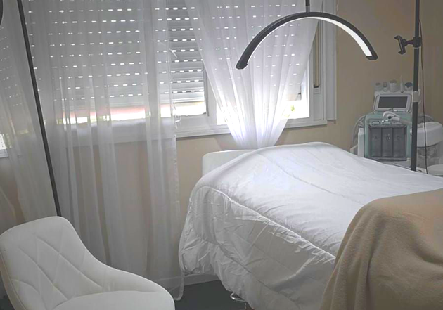 Una sala de tratamiento con una camilla de masaje, ropa de cama blanca, una luz anular curva