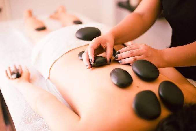 Durante un tratamiento de spa, un masajista coloca piedras lisas, oscuras y calientes sobre la espalda de una persona.