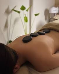 Durante un tratamiento de spa, un masajista coloca piedras lisas, oscuras y calientes sobre la espalda de una persona.